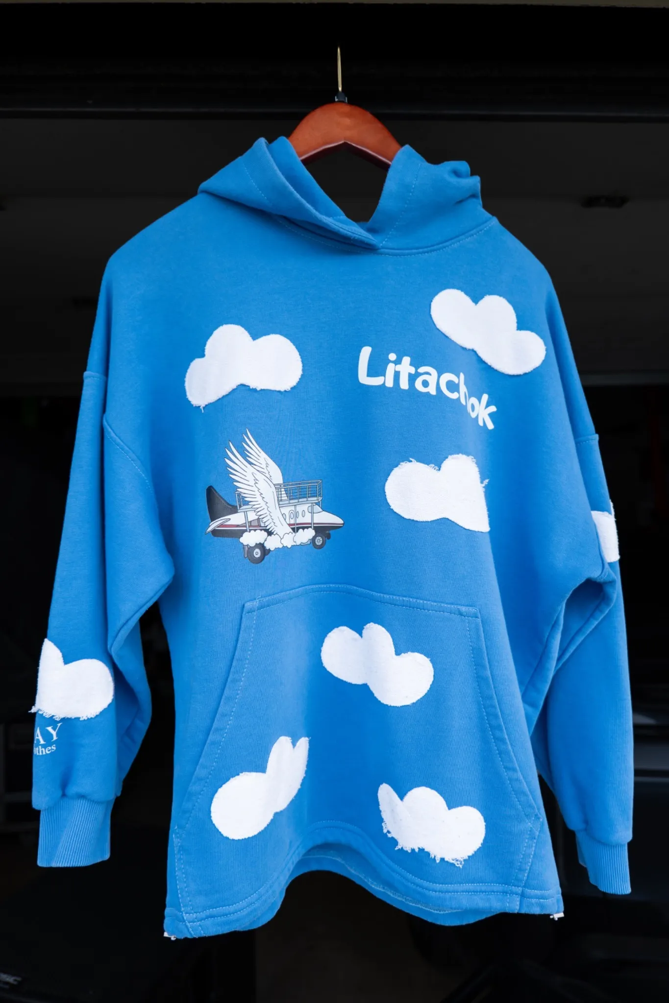 Blue oversized Litachok hoodie with white clouds and an aircraft illustration.